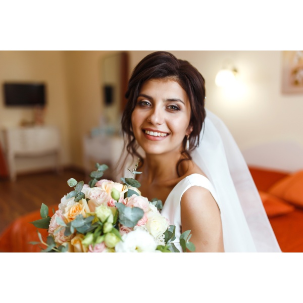 Morning of bride. Beautiful smiling brunette bride in white dress with wedding bouquet in her hands.
