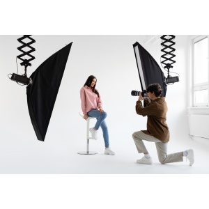 Professional photographer taking picture of young woman, having photoshoot in studio with lighting