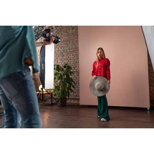Young photographer taking picures of model, backstage of photoshooting in studio.
